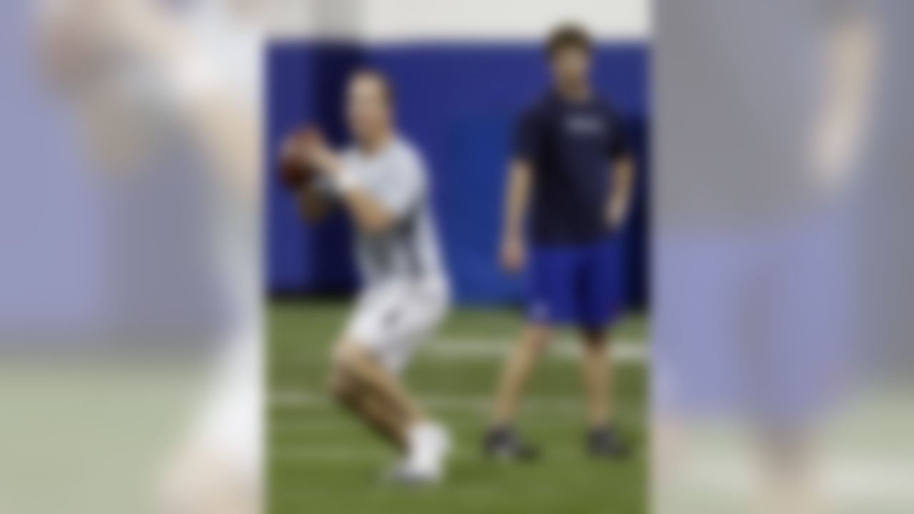 Denver Broncos quarterback Peyton Manning, left, passes as brother Eli Manning, quarterback for the New York Giant, watches at rear during football workouts at Duke University in Durham, N.C., Thursday, April 11, 2013. (AP Photo/Gerry Broome)